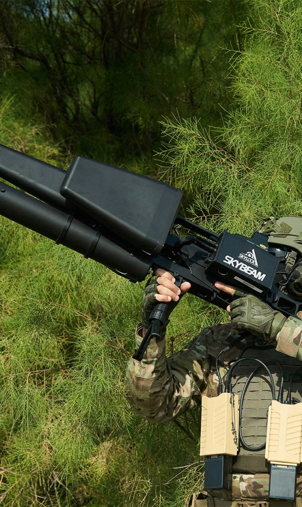 Soldado utilizando um sistema de interferência de radiofrequência, conhecido como Skybeam, para neutralizar drones, em um ambiente de vegetação.